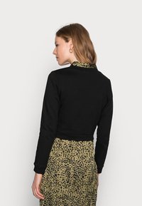Sweatshirt cropped preto com mangas longas, combinado com um vestido verde com padrão de leopardo. O tecido parece suave com um design ajustado.