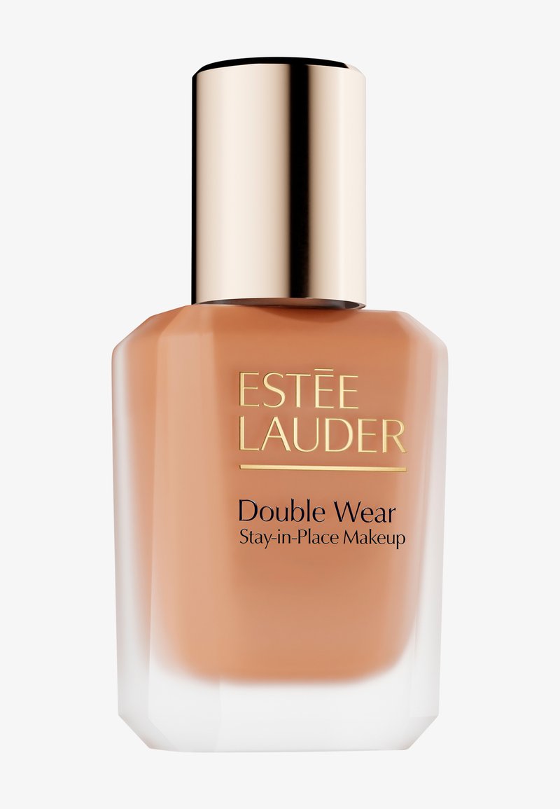 Fond de teint Estée Lauder Double Wear Stay-in-Place dans un flacon en verre transparent avec une base aux tons pêche et un bouchon doré réfléchissant ; design élégant et angulaire.