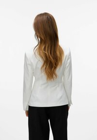 Blazer blanco a medida con mangas largas, ajuste estructurado y textura suave. Presenta un diseño limpio con una costura central en la parte posterior.