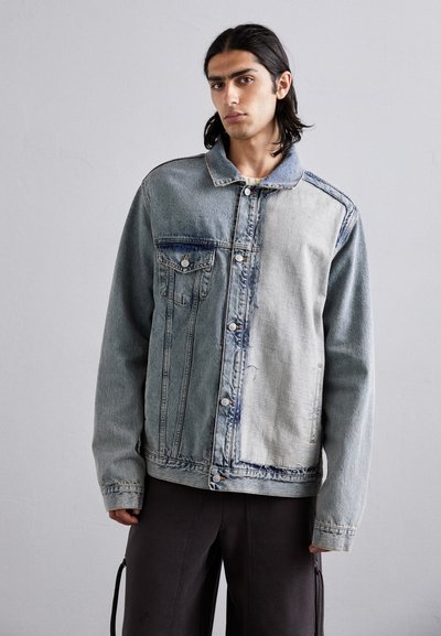 Denim jacket with a faded blue hue, featuring two chest pockets, contrasting textures, and a button-up front. Raw edge detailing at the hem.