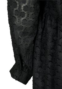 Vestido negro de tela texturizada con patrones circulares elevados, mangas largas y puños abotonados para un detalle adicional.