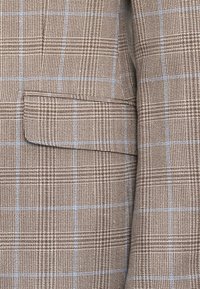 Καφέ καρό ύφασμα με ανοιχτό μπλε γραμμές, διαθέτοντας λεπτομέρεια τσέπης; υφαντή επιφάνεια με δομημένο σχέδιο πλέξης.