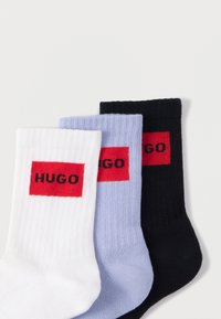 Kolm paari sokke: valged, helesinised ja mustad, igaühel punane ristkülikukujuline logo, millel on musta värviga kiri "HUGO". Sooniline tekstuur.