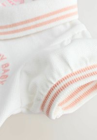 Valge kangas, millel on tekstuuriga pind, roosade triipudega varrukatel ja peene broderi. Pehme materjal, kogutud detailid servades.
