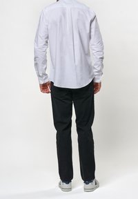 Vit långärmad skjorta med rundad nederkant, tillsamans med svarta byxor och vita sneakers. Tyget verkar slänt; skjortan har en detalj med rygggarn.