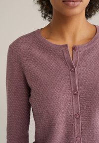 Knopenvest in een gestructureerde paarse brei, met een ronde halslijn en vijf bijpassende knopen aan de voorkant.