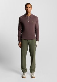 Polo da uomo bordeaux a maniche lunghe con texture a coste, colletto a tre bottoni e piccolo logo. Abbinato a pantaloni verde oliva e sneakers bianche.