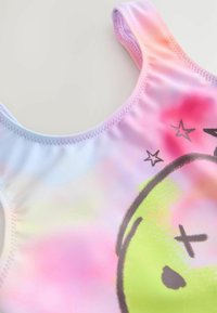 Maillot de bain multicolore présentant un dégradé de teintes pastel avec un grand smiley vert en graphic et des accents d'étoiles noires. Texture de tissu lisse.