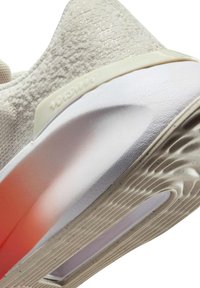 Gaiši pelēki sporta apavi ar faktūrētu augšdaļu, krēmkrāsas akcentiem, pasteļoranžīgu pāreju uz vidussoļiem un viļņveida raksta gumijas zoli.
