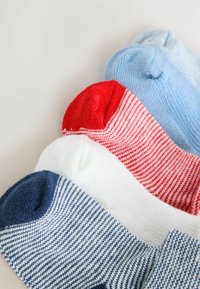 Cztery pary skarpetek kostkowych w kolorach niebieskim, białym, czerwonym i jasnoniebieskim, ułożone w ukośnym rzędzie na białej powierzchni.