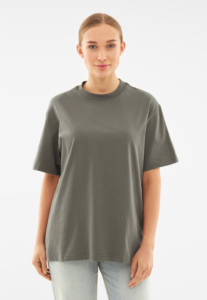 Grijze T-shirt met korte mouwen, ronde hals, relaxte pasvorm. Gemaakt van katoen, met een zachte textuur. Gepaard met lichtblauwe jeans.