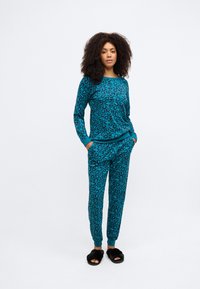 Tyrkysová sada pyžama s leopardím vzorom, vyrobená z mäkkej látky. Obsahuje vrchný diel s dlhými rukávmi a zúžené nohavice s manžetami.