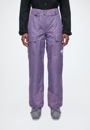 Un mannequin porte un pantalon de ski couleur lavande avec des poches cargo et des genoux renforcés, assorti à une veste noire et à des chaussures de ski grises.