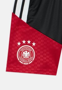 Punane ja must spordilühi, kus on kolm musta triipu, Saksamaa Jalgpalliliidu logo ja neli valget tähte. Tekstuuriga kangas.