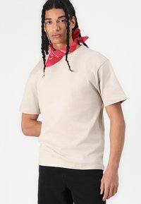 Camiseta de algodón beige con mangas cortas y un corte relajado, combinada con una bandana roja con patrones blancos.