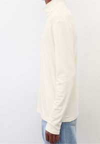 Langärmliges Rollkragenshirt in Elfenbein, aus weichem Stoff gefertigt. Verfügt über ein tailliertes Design mit glatter Textur und hohem Kragen.