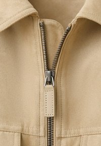Beige suede jacket with a partially unzipped silver metal zipper and wide collar.