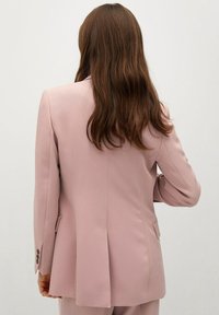 Jasnoróżowa, dopasowana marynarka wykonana z usztywnionej tkaniny, z pojedynczym rozcięciem z tyłu, długimi rękawami i zapinanymi na guziki mankietami.