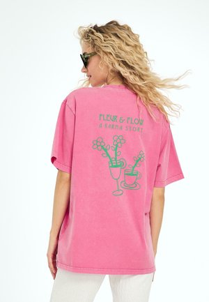 T-shirt en coton oversized rose avec un design graphique de fleurs dans des tasses au dos, avec des accents verts et une coupe décontractée.