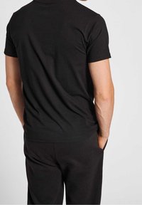 Czarny t-shirt z krótkim rękawem wykonany z miękkiej bawełny, z klasycznym okrągłym dekoltem i gładką teksturą, widok od tyłu.