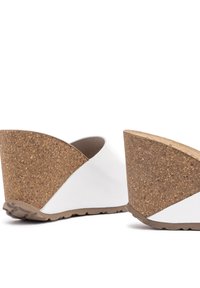 White wedges with a cork heel feature a triangular design. The upper has a smooth texture, while the heel has a natural cork finish.