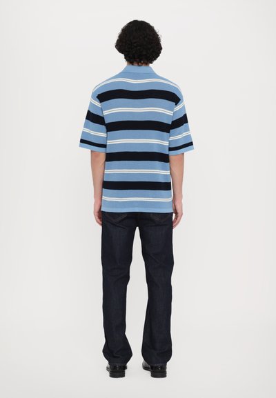 Kortermet, skjorte med krage i lyseblå, marineblå og hvite horisontale striper; brukt med mørkeblå jeans; strukturert strikket stoff.