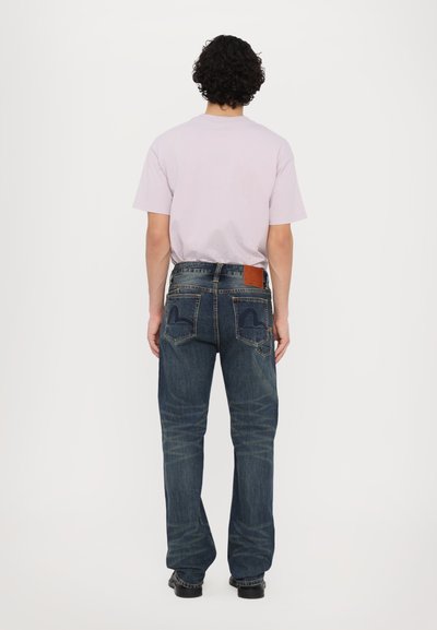 Jeans en denim bleu foncé avec une coupe droite, présentant des poches arrière avec des accents brodés et une patch en cuir à la taille.