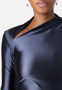 Marineblå satin top med diagonalt udskåret ved halsen, lange ærmer og en glat, tætsiddende tekstur.