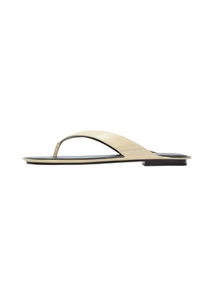 Sandale plate beige à lanière avec une semelle fine et un talon noir minimaliste, montrée de profil sur fond blanc.