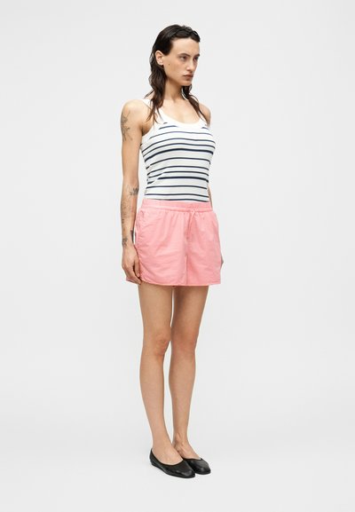 Ριγέ τοπ με μπλε και λευκές γραμμές, συνδυασμένο με ροζ σορτς με ελαστική μέση και μαύρα επίπεδα παπούτσια. Ομαλή υφή υφάσματος.