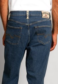 Jeans in denim blu scuro con design dritto, caratterizzati da un'etichetta del marchio sul retro e cuciture decorative sulle tasche.