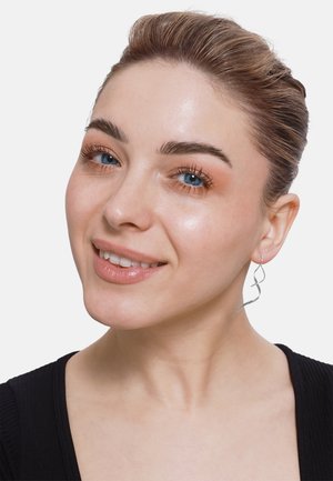 Srebrne spiralne uhane s zavitim dizajnom, ki se nežno zibajo. Model ima gladko kožo in nosi črn top.