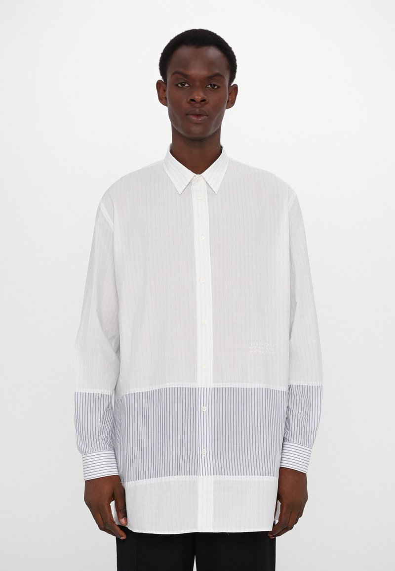 Chemise blanche à boutons, ornée de rayures verticales blanches et bleues, avec un col évasé et des manches longues à poignets rayés.