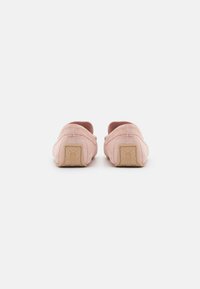 Rosa semskede slip-on sko sett bakfra, med runde hæler og en teksturert, beige gummi såle med preget detalj.