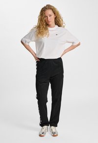 Biała bawełniana koszulka z okrągłym dekoltem i krótkimi rękawami, zestawiona z czarnymi spodnimi o zwężanych nogawkach, z bocznymi paskami i elastycznym pasem.