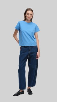 Niebieska bawełniana koszulka z krótkim rękawem, w połączeniu z luźnymi, ciemnoniebieskimi dżinsami i czarnymi butami typu slip-on. Prosty design, bez wzorów.