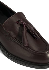 Bruine leren instapper met een gladde textuur, voorzien van dubbele kwastjes en een gestructureerde zwarte rubberen zool. Geen zichtbare stikdetails.