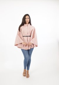 Ljusrosa kappa med hög krage, försedda med knäppning, tillsammans med ett svart bälte, bärs över blå tajta jeans och genomskinliga klacksandaler.