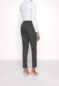 Grijze, gestructureerde broek met een slim fit en opgerolde boorden, gecombineerd met een witte langemouwen top en witte hakken. Twee achterzakken zichtbaar.