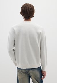 Suéter gris claro hecho de un material suave, con un escote redondo y puños acanalados, combinado con jeans azules desgastados. Vista trasera.