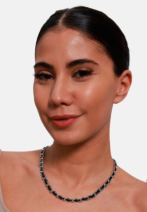 Collana a catena argento e nero con anelli intrecciati, indossata da un modello su sfondo bianco puro.