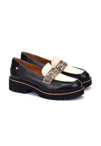 Mocasines de cuero negro y crema con una suela negra gruesa, que presentan una correa decorativa marrón y detalles de metal dorado.