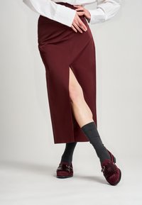 Falda midi burdeos con abertura lateral, combinada con calcetines oscuros hasta la rodilla y zapatos burdeos con un detalle de correa decorativa y textura.