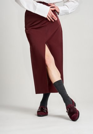 Gonna midi bordeaux con spacco laterale, abbinata a calze al ginocchio grigio scuro e scarpe bordeaux con una fascia decorativa e dettagli di texture.