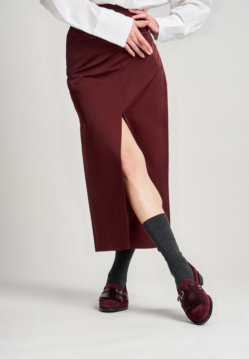 Gonna midi bordeaux con spacco laterale, abbinata a calze al ginocchio grigio scuro e scarpe bordeaux con una fascia decorativa e dettagli di texture.