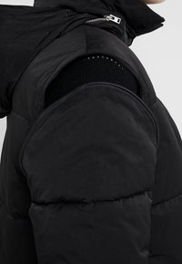 Chaqueta de plumas negra con apertura con cremallera en la manga, diseño estructurado, acabado mate y textura acolchada en toda la prenda.