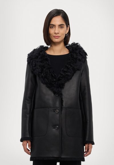 Abrigo de cuero negro con un cuello de piel rizada negra, con cierres de botón y dos bolsillos frontales. Textura suave con un ajuste estructurado.