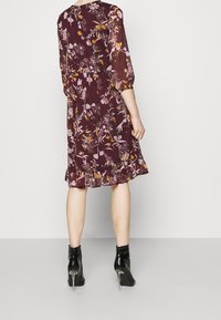 Tummanpunainen kukkakuvioinen mekko, jossa on kolme neljäsosaa hihat, liehuva helma ja kevyt kangas. Yhdistetty kiiltäviin mustiin nilkkureihin, joissa on korkea korko.