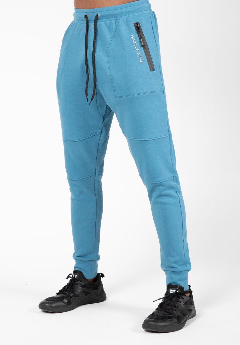 Lichtblauwe joggingsbroek van zachte stof met zwarte accenten. Kenmerken zijn onder andere een ritszak en een koordband.