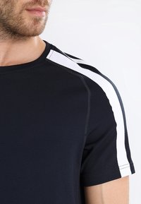 Schwarzes Sport-T-Shirt aus strukturiertem Stoff mit weißen und grauen Streifen auf den Schultern. Rundhalsausschnitt und kurze Ärmel.